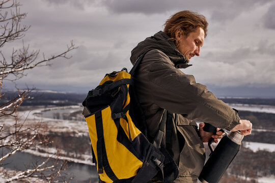 Man hiker hiking in mountain forest going to drink tea from thermos wearing cold weather accessories, wind jacket for camping outdoor. Guy portrait lifestyle. caucasian male relax, have rest