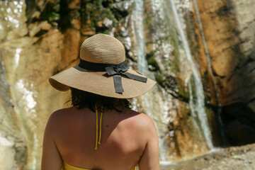 Woman in the hat standing by the waterfall. Shot from behind.
