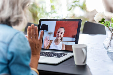 Grandmother speaking on videocall with her granddaughter using laptop at home.