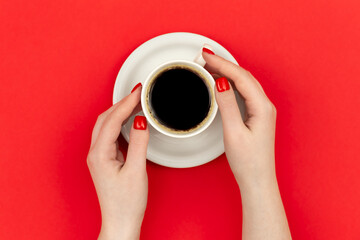 Female hands holding a cup of coffee on a red background, flat lay, minimalism concept.