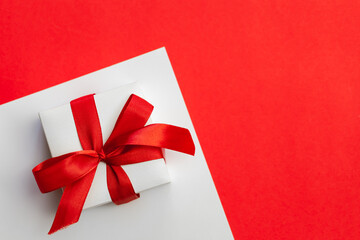 Gift box with a red bow on a red background, flat lay, Valentine's day concept, festive minimalistic background, copy space.