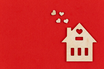 Obraz na płótnie Canvas Wooden house with decorative hearts on a red background, flat lay, space for text.