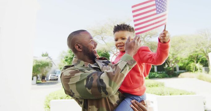 Happy african american father with son embracing and waving flag of usa