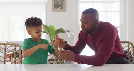 Happy african american man and his son sitting at table and speaking sign language - Powered by Adobe