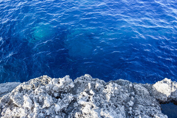 View from over the edge of a rocky cliff to clear blue sea water below