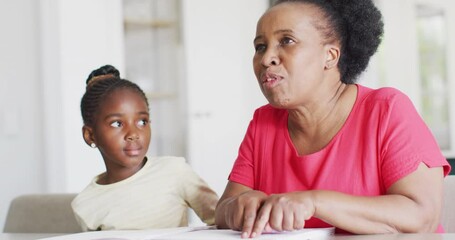 Video of african american granddaughter listening to her smiling grandmother reading braille