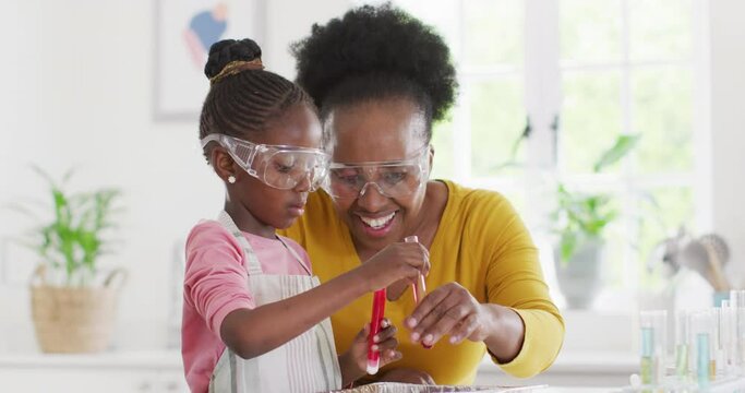 Excited african american granddaughter and grandmother make chemistry experiment at home, copy space