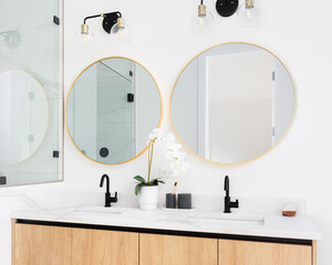 A beautiful bathroom with a wood cabinet, marble countertop, and gold circular mirrors.
