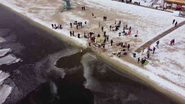 the drone flies over the hole in the winter river, the river is covered with ice, people enter the cold water, cross themselves and plunge headlong into the ice water three times
