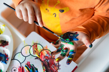 a happy little girl paints her hand with colored paints a girl in an orange blouse with a giraffe