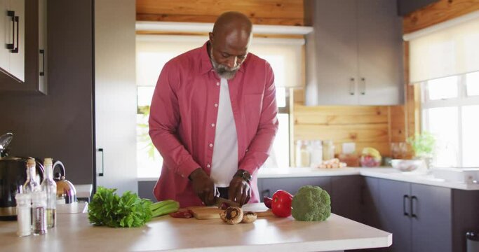 Happy senior african american man spending time in log cabin, cooking in kitchen