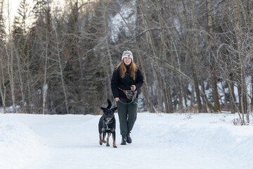 Fototapeta na wymiar woman with dog walking in the snow in the winter on a trail