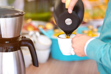 Close up of man pouring coffee from a coffee pot. Black coffee on a white cup.