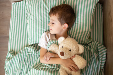 adorable boy sleeping in bed with bear toy. six year old baby sleeping at home. sleeping baby portrait from above