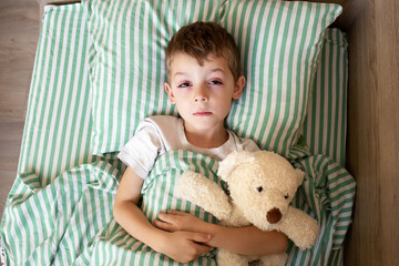 Unhealthy little boy child sleep in bed at home in bedroom. Sick ill little kid suffer from flu fever asleep in bed on lockdown quarantine. portrait of a sick child. sick child hugging a teddy bear