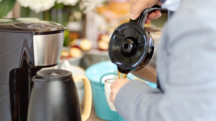 Close up of man pouring coffee from a coffee pot. White cup filled with black coffee.
