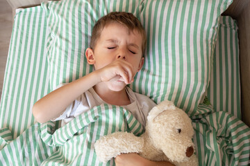 Unhealthy little boy child sleep in bed relax at home in bedroom. Sick ill little kid suffer from flu fever asleep in bed on lockdown quarantine. portrait of a coughing child