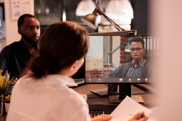 Teamlead listening to employee report presentation on corporate videocall, online business meeting. Company briefing, coworkers chatting on teleconference in coworking space at night