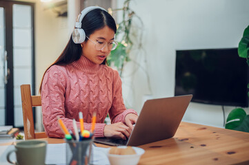 Vietnamese Asian woman using laptop and headphones while working from home