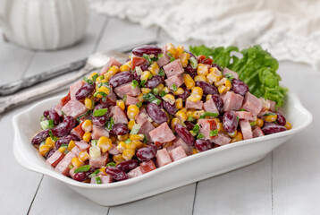 Colorful Corn Salad with Ham and Kidney Beans served in a white bowl on a light wooden background. Selective focus, horizontal.