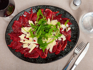 Beef carpaccio with slices of cheese served with arugula on table in restaurant.