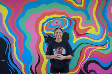 beautiful woman, woman holding paintbrush and standing in front of painted wall. painted colorful wall art