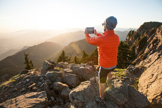 A hiker uses a tablet to take a picture of the sunset.