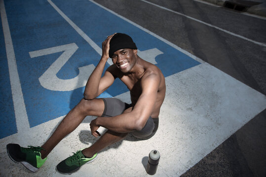 Portrait of shirtless athlete sitting on all-weather running track and smiling, Barcelona, Spain