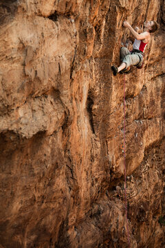 Caucasian male climber leading a trad line up a sandstone cliff in Badami, India.