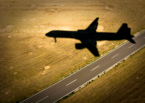 The shadow of an airliner crosses an empty road as it approaches the runway.