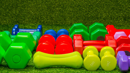 multi-colored dumbbells on a background of green grass - obrazy, fototapety, plakaty