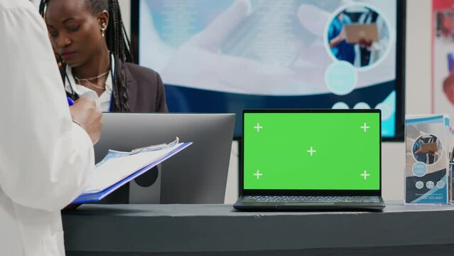 People working with greenscreen display on laptop in facility lobby, using checkup form papers in health center. Isolated chroma key display with blank mockup template and copyspace on front desk.