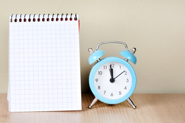 Empty notepad page with alarm clock on desk