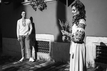black and white photo, Emotional portrait of happy young couple in love, family hugging, holding hands, running in Lviv city in traditional Ukrainian shirts. Young people hug in the old town of Lviv