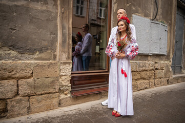 Fototapeta na wymiar Portrait of a happy young couple in love, a family hugging, holding hands in the city of Lviv in traditional Ukrainian shirts, holding hands. Young people hug in the old town of Lviv