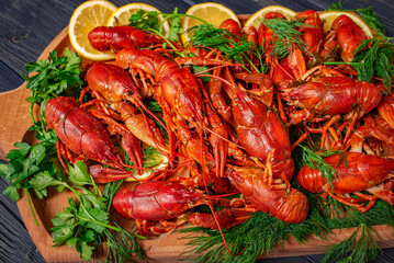 Red boiled crayfish with lemon and dill on a wooden board. Tasty crayfish on a black wooden background.