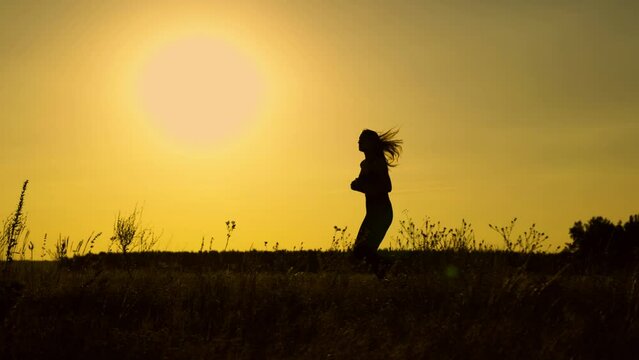 Running after sun. Training jogging. A healthy beautiful girl is engaged in fitness, jogging in country in sun. Jogger girl breathes fresh air on field. Free young woman runs in summer park at sunset.