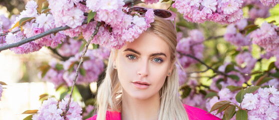 Fototapeta premium Sensual woman near sakura tree background, banner for website header. Spring girl. Outdoor portrait of young beautiful happy smiling female model near flowering tree.