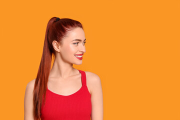Obraz premium Happy woman with red dyed hair on orange background, space for text