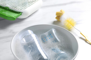 Bowl with baby bottles on white marble table in kitchen