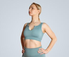 A young blonde girl in yoga clothes stands in a hero pose. Proud strong woman in sportswear