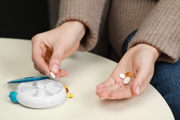 Woman taking pill from plastic container at white table, closeup