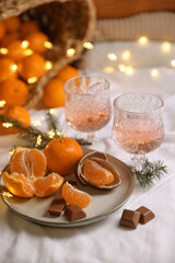 Delicious ripe tangerines, chocolates, festive lights and glasses of wine on white bedsheet