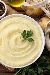 Bowl of tasty mashed potato, parsley, olive oil and pepper on wooden table, flat lay