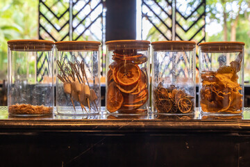 Dried sliced oranges lie in a transparent glass jar next to other dried fruits.