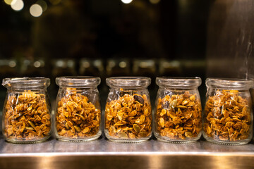 Small portion glass jars of granola stand in a row on the shelf 