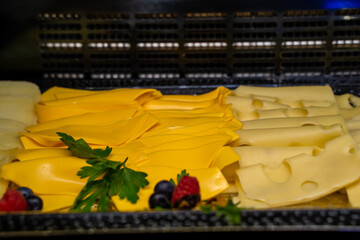 Sliced cheese lies on a tray, bright and dull yellow, next to the greens
