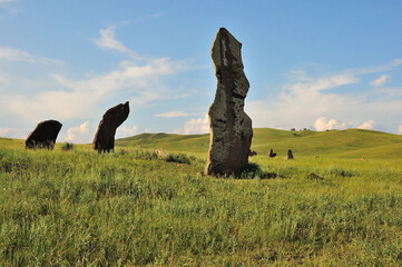 A group of ancient burial stones on the slopes of a hilly valley on a sunny summer day.