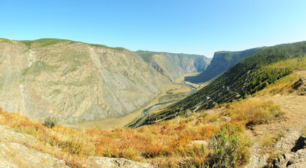 Panoramic view of a picturesque autumn valley with a flowing river and a steep winding road down.