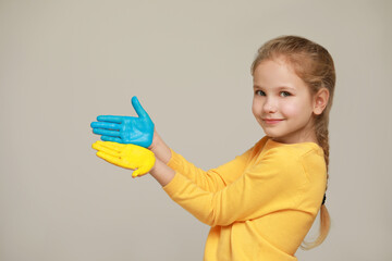Little girl with hands painted in Ukrainian flag colors on light grey background, space for text. Love Ukraine concept